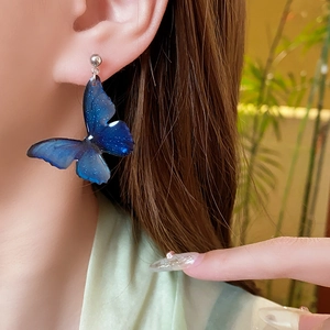 Detailed view of deep blue butterfly stud earrings with silver pins on female model
