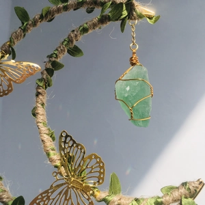 Macro detail of natural green crystal pendant with gold wire wrap and leaf decor