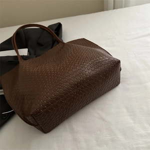 Brown woven tote bag with large capacity in retro minimalist style on a white bed