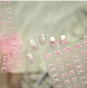 Macro detail of 3D pink bow nail stickers and white gradient manicured nail samples
