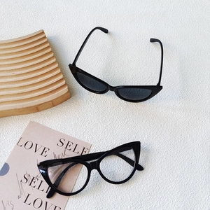 Classic black cat-eye kids sunglasses and clear glasses on a wavy wooden tray