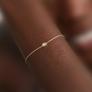 Close-up of a minimalist gold chain bracelet featuring an eye-shaped pendant with a zircon