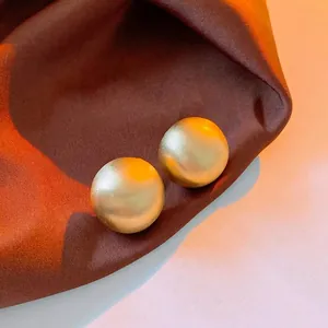 Pair of minimalist matte gold spherical stud earrings on premium dark brown silk fabric