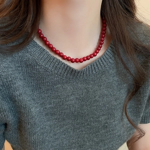 Detailed view of red glass bead necklace on a model wearing a grey sweater