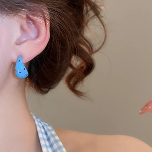 Close-up of blue C-shaped earrings with red polka dots worn by a model in soft light