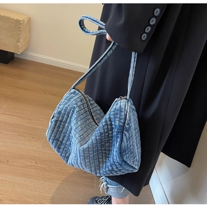 Detailed view of the blue quilted denim shoulder bag with soft curved design on a model