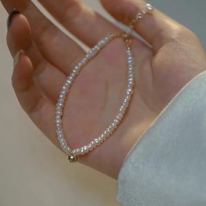 Detailed close-up of a natural pearl necklace with a small gold ball charm on a model's hand