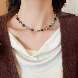 Detail of vintage tiger eye and pearl necklace on model with golden metal accents