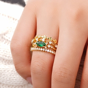 Vista macro detallada de cuatro anillos dorados apilables con una piedra verde de corte marquesa