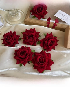 Macro shot of red velvet rose hair clips and brooches with green leaves on silk fabric