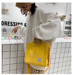 Detail of yellow corduroy crossbody bag with adjustable strap and logo patch in a cafe setting