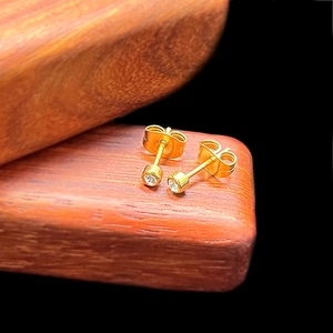 Detailed view of mini round zircon stud earrings with gold finish on a wood base