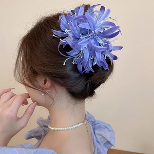 Élégante pince à cheveux fleur en tissu violet avec pompons portée par femme aux longs cheveux