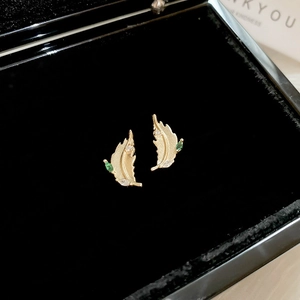 Detail view of gold leaf earrings with green and white zircons on black velvet case