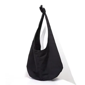 Detail of black canvas hobo bag featuring a knotted strap design and sleek curved shape