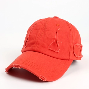 Close-up of distressed red cotton baseball cap with ripped holes and frayed vintage details