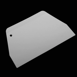 Close-up of white plastic scraper tool with trapezoid design and ergonomic handle