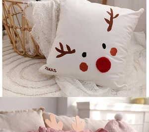 Close-up of white plush Christmas pillow with reindeer embroidery and 3D red nose detail