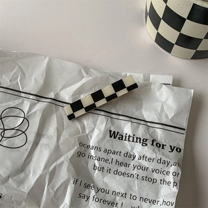 Close-up of a rectangular black and white checkered hair clip on a paper background