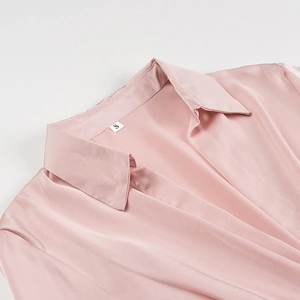 Detailed close-up of pink satin V-neckline texture and size label on long sleeve dress