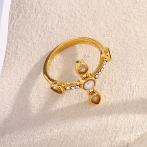 Macro detail of 18K gold-plated cross ring with pearl center and sparkling crystals