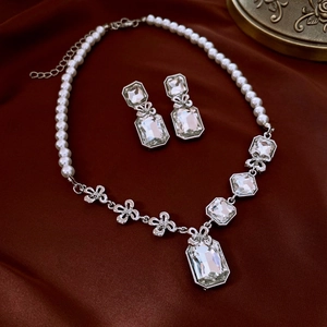 Détail du parure collier et boucles d'oreilles perles et fleurs en cristal sur soie rouge