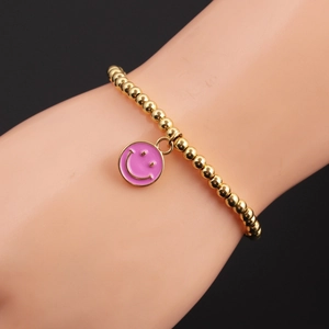 Detail of gold beaded bracelet featuring a pink enamel smiley face charm on a model hand