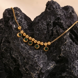 Macro shot of 18K gold plated steel anklet with green gemstone on dark volcanic rock