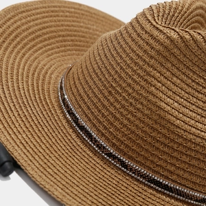 Close-up of woven straw sun hat with snake pattern band and rhinestone detailing