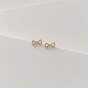 Macro detail of gold bow stud earrings featuring delicate beaded metal texture on paper