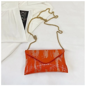 Detail of orange crocodile texture handbag with elegant gold chain strap on a magazine