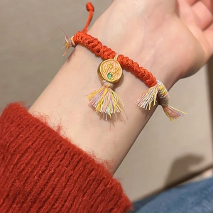 Gros plan du bracelet chanceux tressé rouge avec pendentif émail et gland en soie
