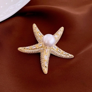 Détail d'une broche étoile de mer dorée avec une perle blanche et des zircons brillants
