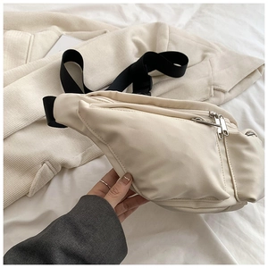 Detail of cream white fabric crossbody bag featuring dual silver metal zippers and strap