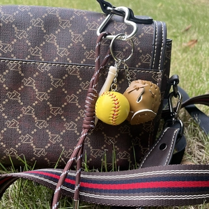 Detailed shot of a yellow baseball, brown glove, and wood bat keychain on a brown bag