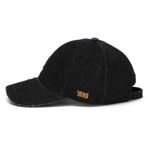 Detail of vintage black denim baseball cap with orange 1999 embroidery and distressed brim