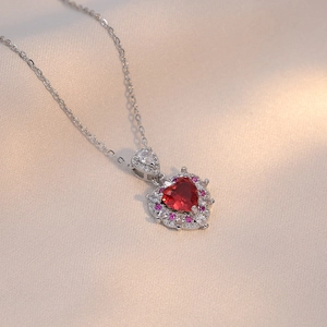 Women's heart pendant necklace with red zircon and silver chain on silk background
