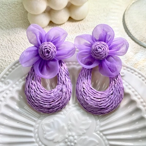 Close-up of purple woven straw earrings with tulle flower petals on a white ceramic plate