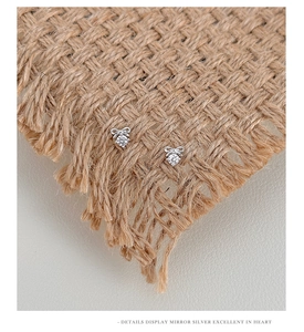Macro detail of silver bow earrings with zircon stone on a textured fabric base