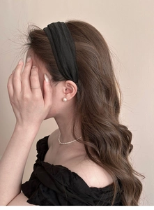 Detail view of a black pleated headband with texture on a model with elegant pearl jewelry