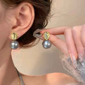 Détail de boucles d'oreilles pendantes en perle grise et cadre doré sur mannequin