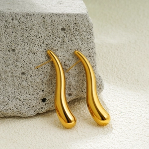 Macro shot of 18K gold water drop earrings on a natural grey rock and white sand background