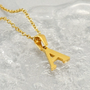 Collier avec pendentif lettre A en acier inoxydable doré sur fond gris texturé