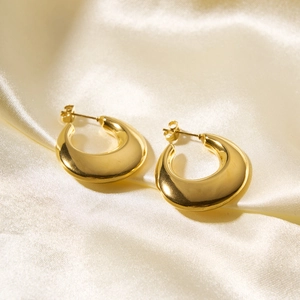 Close-up of polished gold hollow hoop earrings on soft beige silk fabric with soft lighting