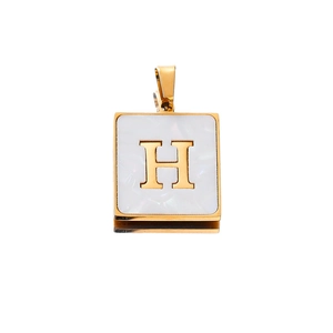 Close-up of golden square pendant featuring white shell inlay and 3D metal letter H