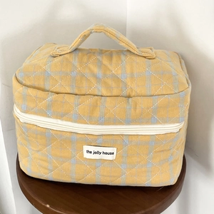 Detailed close-up of yellow plaid quilted fabric and white logo on the cosmetic bag