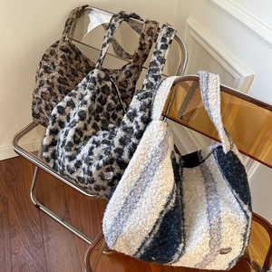 Three plush leopard and striped tote bags stacked on a clear chair in a cozy home setting