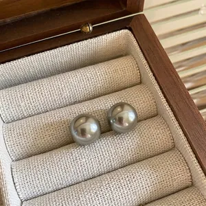 Macro detail of glossy grey pearl stud earrings on a cream woven jewelry box pad