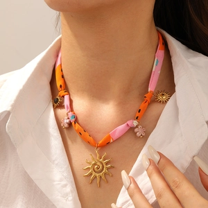 Détail de pendentifs soleil et fleur dorés sur un collier en cordon de tissu tie-dye coloré