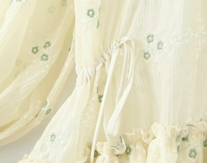 Dettaglio macro del tessuto a righe beige con ricamo floreale e coulisse regolabile in vita
